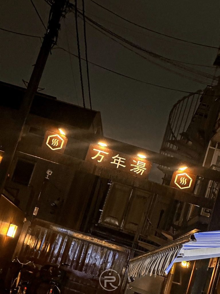 [發光萬年湯木招牌]： 仰拍萬年湯木質大門樑上的立體發光店名標誌。
