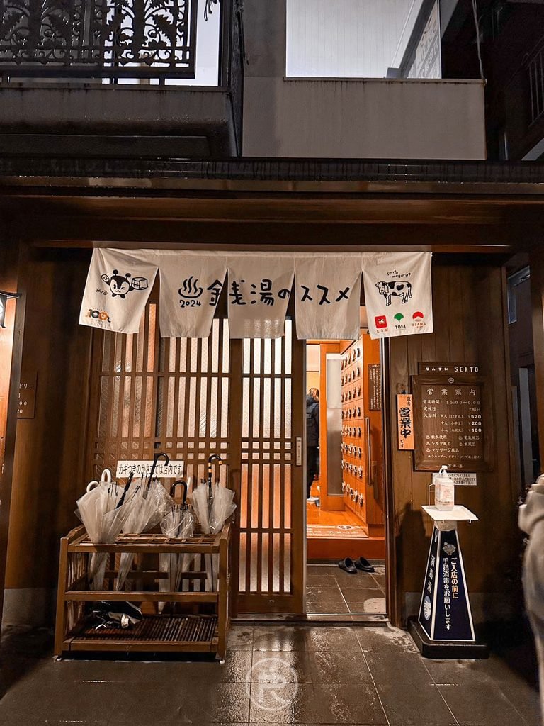[正門白色日式暖簾]： 萬年湯正門入口處懸掛「自然と健康の湯 万年湯」白色日式暖簾與木質拉門。