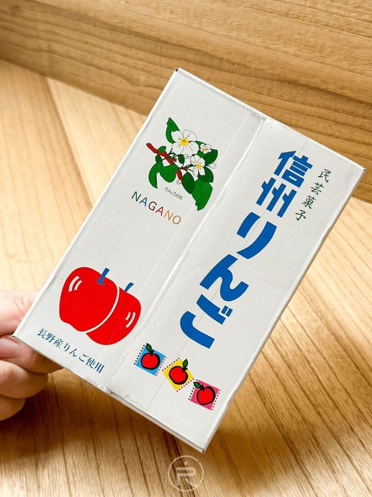  [手拿外盒特寫]： 手持展示紙盒正面，標示「長野縣產蘋果使用」與蘋果花手繪圖案。