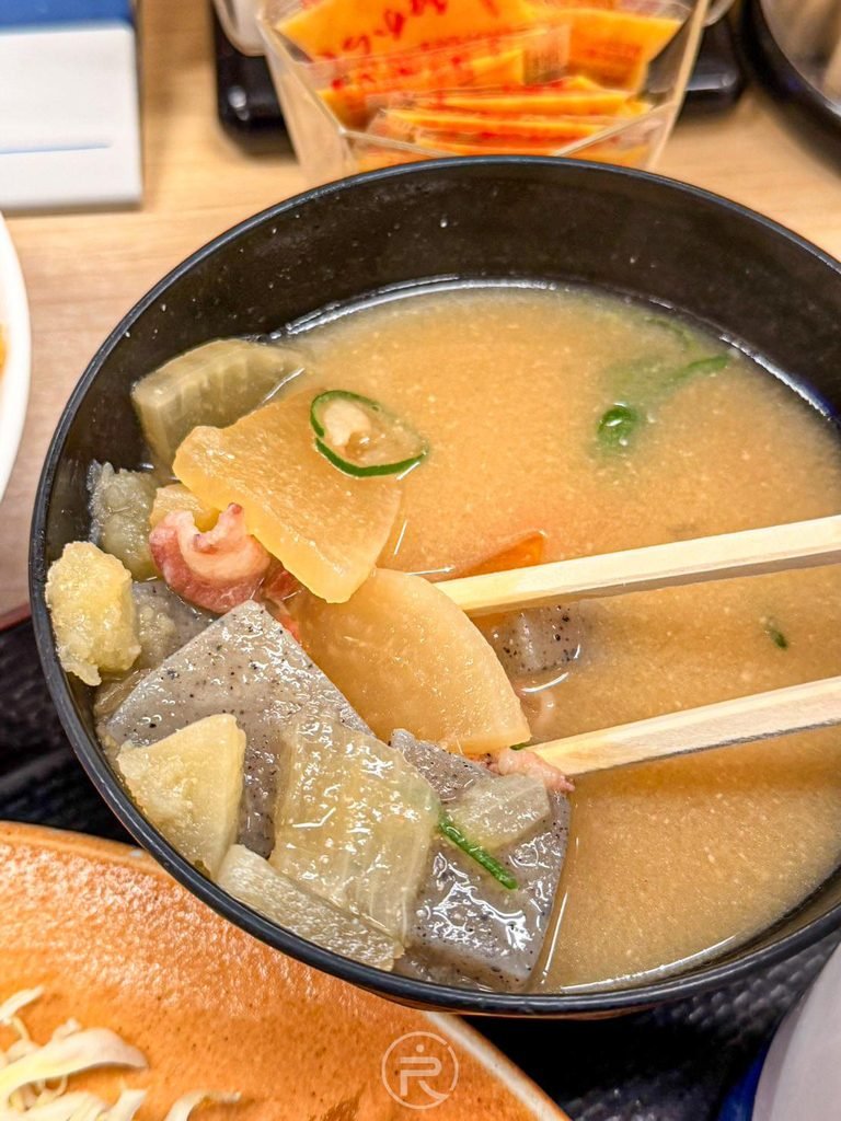 [豚汁滿滿配料]： 筷子舀起附餐蔬菜豬肉味噌湯（豚汁），滿滿的大塊蒟蒻、白蘿蔔與五花肉片。
