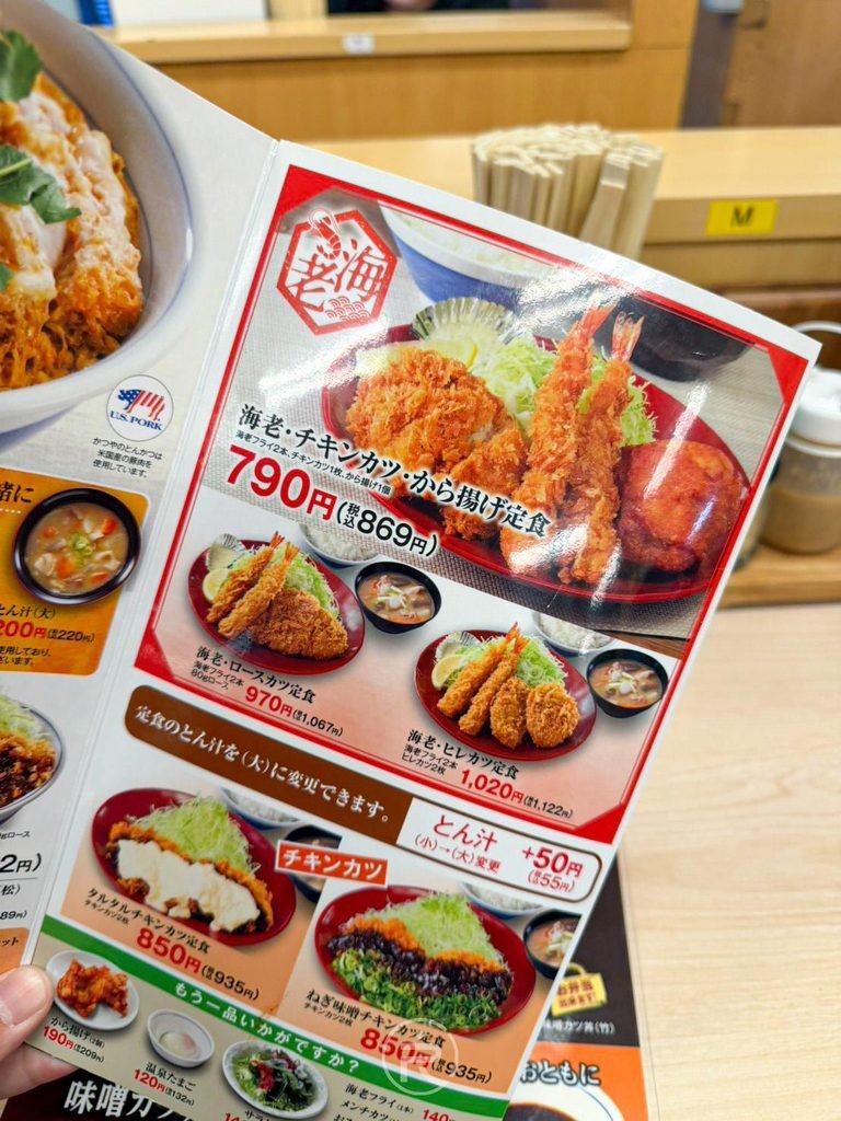 [手持桌上菜單本]： 手持展示店內常設紙本菜單，清楚標示各類炸豬排丼與定食價格。
