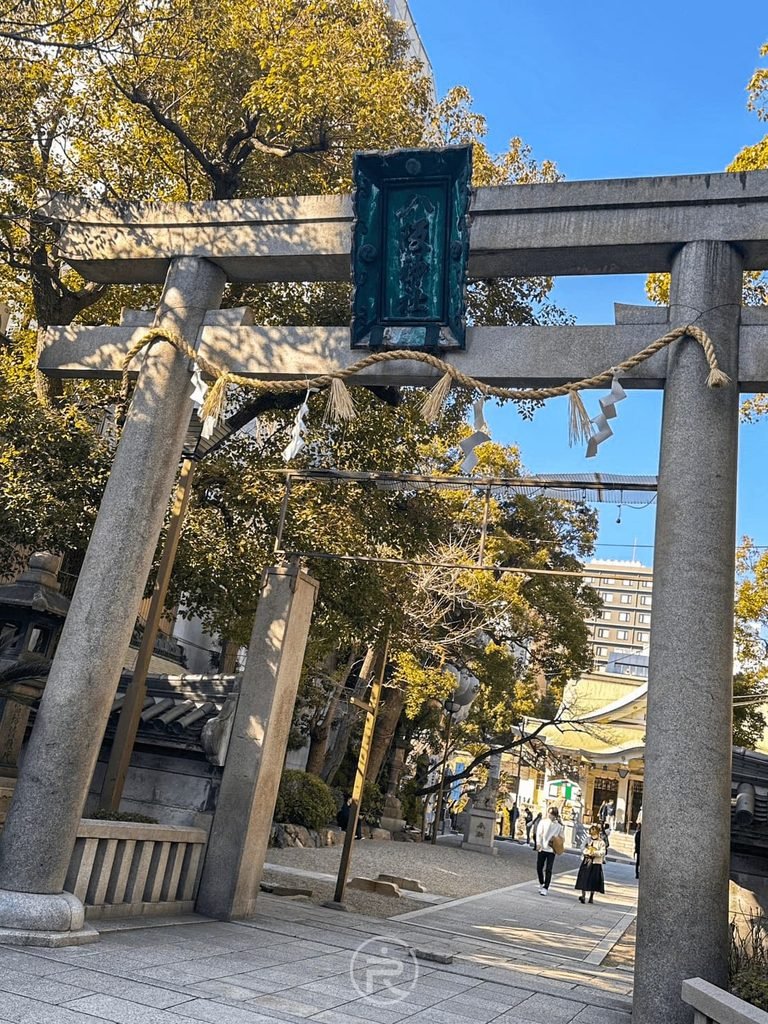 [石造鳥居參道]： 難波八阪神社入口處高大的石造鳥居，兩側為寧靜的住宅街景。