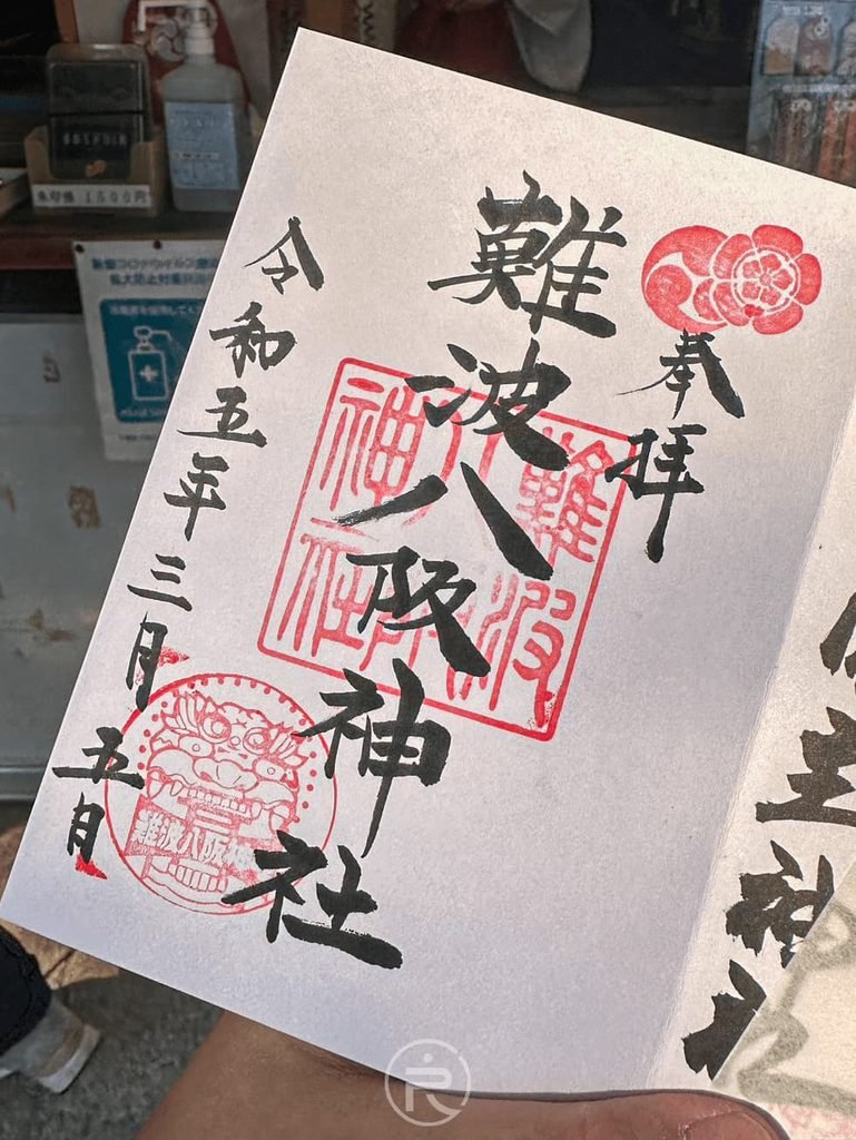  [手持御朱印]： 手持難波八阪神社手寫御朱印紙本，蓋有朱紅社印與春季花草浮水印。