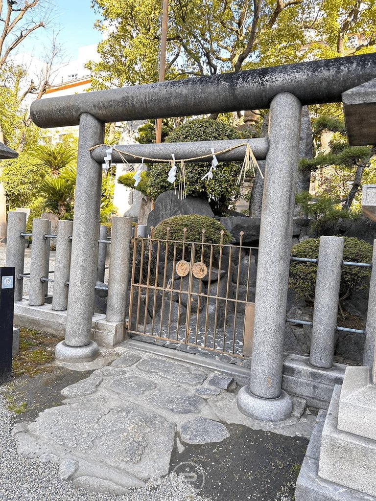  [石造小鳥居]： 境內末社前的石造鳥居與木造圍欄，綠樹環抱氛圍清幽。