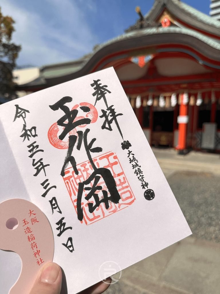 [手持玉造御朱印]： 手持玉造稻荷神社手寫御朱印墨寶，蓋有特色勾玉朱印與紅色拜殿合影