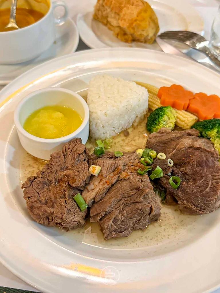 德奧小館 盤中擺放厚實牛胸肉塊、白飯、綠花椰菜、雕花紅蘿蔔與特製沾醬。