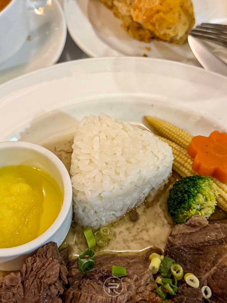  [三角白飯與配菜]： 盤邊可愛的立體三角形白米飯糰，搭配金黃玉米筍與紅蘿蔔花。