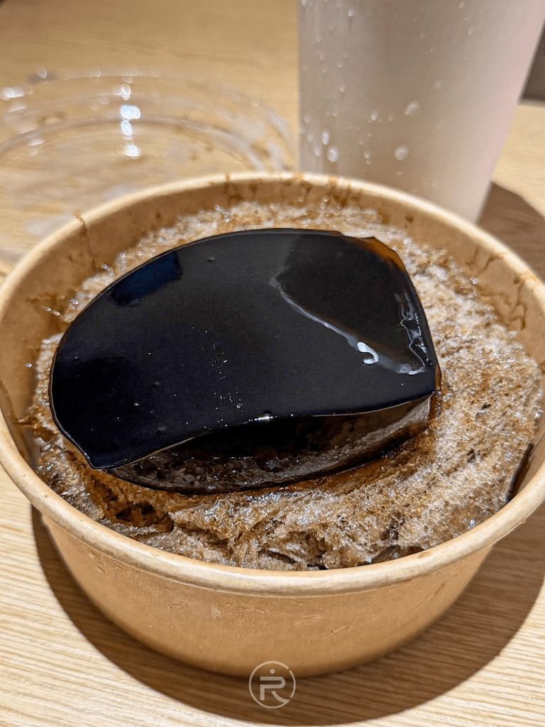 [黑亮仙草凍特寫]： 放在滿滿仙草絲刨冰上的整塊滑嫩純黑仙草凍，色澤如黑曜石般透亮。