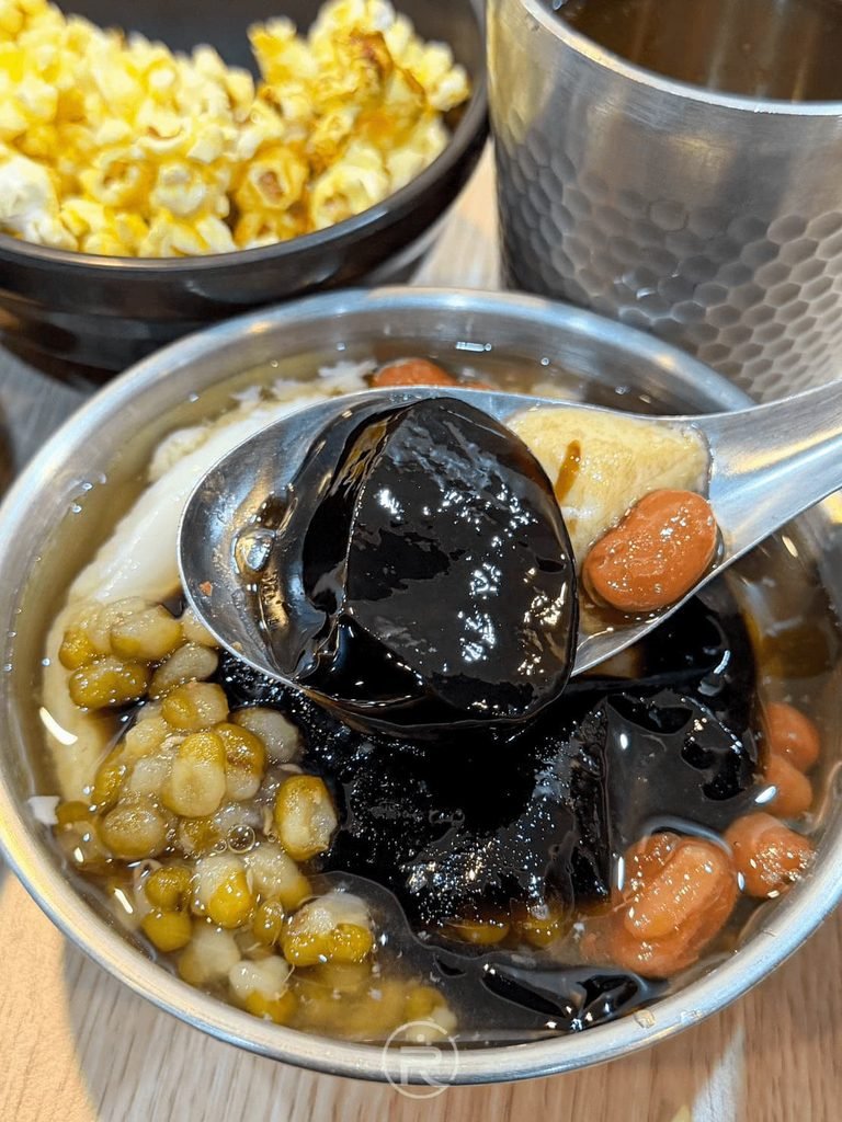 [湯匙舀嫩仙草]： 湯匙舀起滑嫩黑亮的仙草凍，搭配綠豆與香甜糖水。