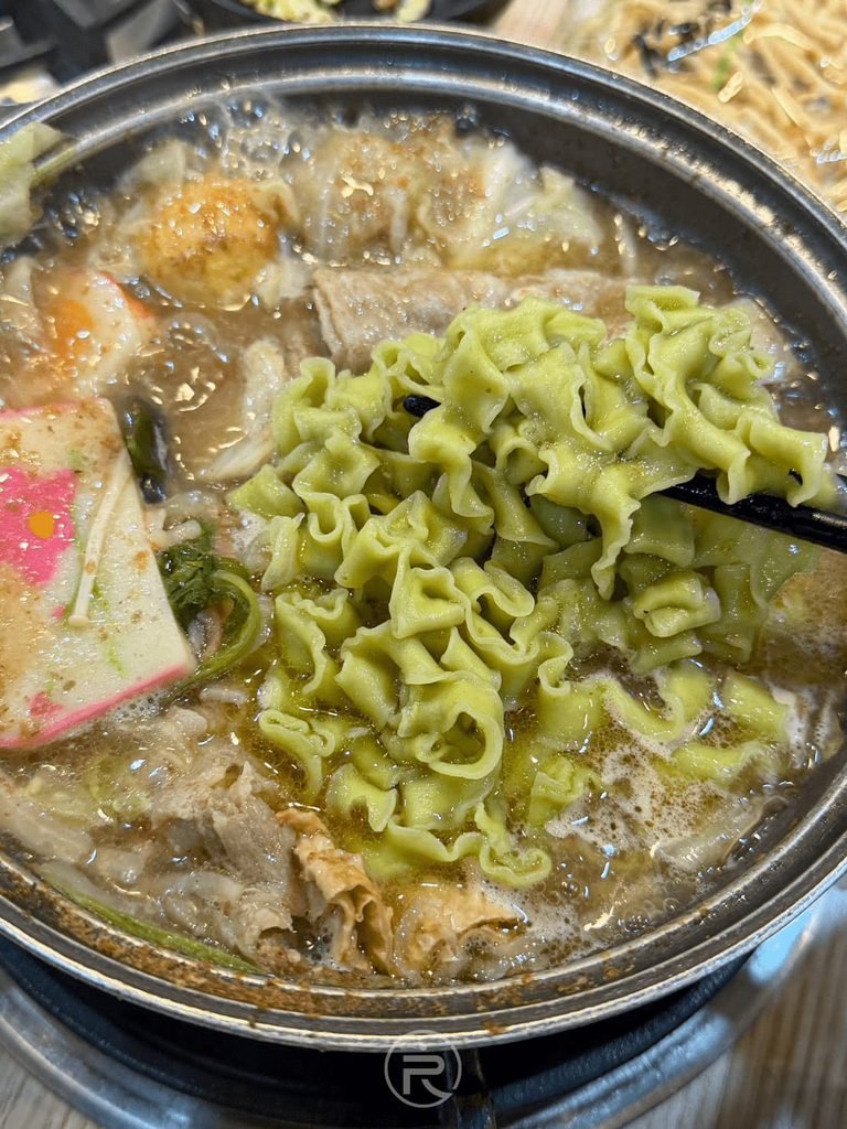 [滾煮波浪麵特寫]： 綠色波浪麵在濃郁沙茶湯中翻滾吸汁，口感 Q 彈有勁。