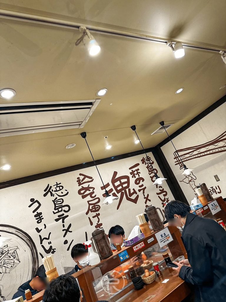 [室內吧檯座位]： 德島拉麵東大店內長型吧檯用餐區，牆上掛滿「德島之魂」木刻匾額。

