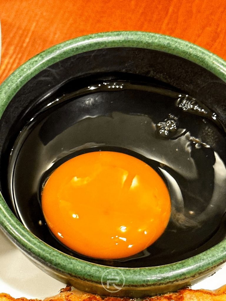  [小碗打生蛋]： 陶瓷小黑碗中打好的鮮橘色生雞蛋，準備倒入拉麵中提味。