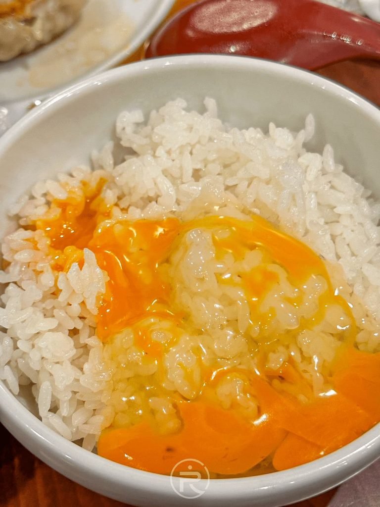  [生蛋拌飯特寫]： 劃破新鮮生蛋黃均勻拌入熱騰騰白飯，呈現誘人的金黃色澤。